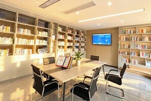 A modern library with bookshelves, a table with chairs, and a television screen. - Homeinn Selected Hotel (Enshi Tusi City ) (Enshi City)