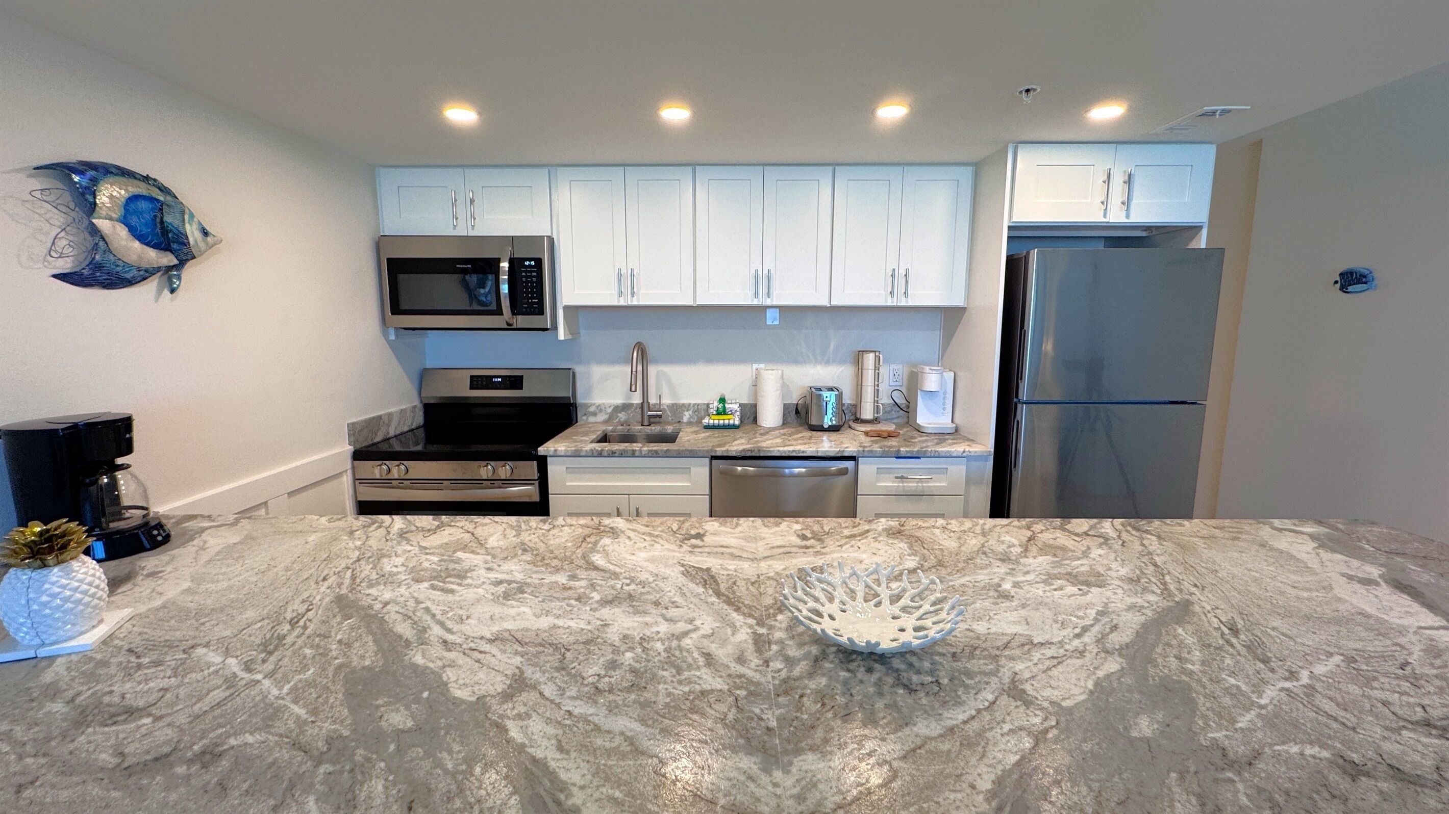 A modern kitchen with white cabinets, stainless steel appliances, and a marble countertop.