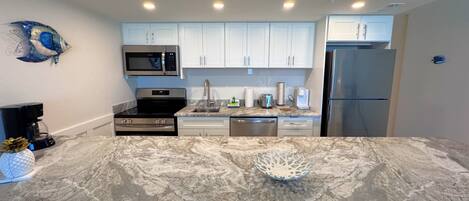 A modern kitchen with white cabinets, stainless steel appliances, and a marble countertop.