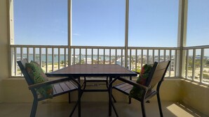 Een balkon met een tafel en twee stoelen, met uitzicht op een kustgebied met gebouwen en een heldere lucht.