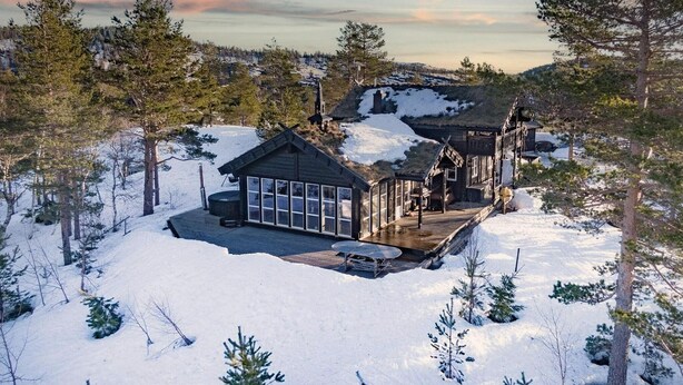 Une cabane dotée d’une grande baie vitr ée, entourée d’un paysage enneigé et d’arbres.