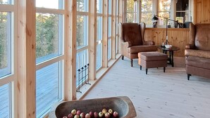 L’intérieur chaleureux d’un chalet, avec ses murs en bois, ses grandes fenêtres, un canapé en cuir marron et une auge en bois remplie de pommes.