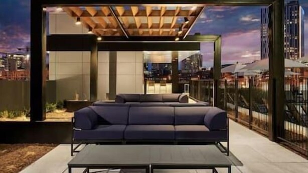 Un espace extérieur moderne, aménagé avec un canapé et une table, offrant une vue sur le paysage urbain au crépuscule.