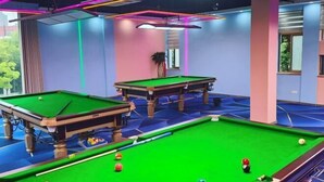 A pool table with balls, a second table, and a potted plant in a room with blue walls and a window. - Changwei Hotel (Shanghai)