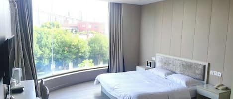 A hotel room with a large bed, bedside tables, a desk, and a view of the city.
