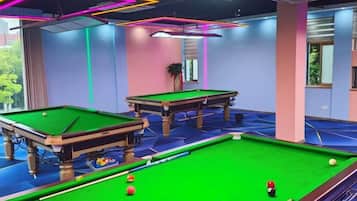 Uma área de jogos com duas mesas de sinuca, superfície de feltro verde e piso coberto por carpete azul.
