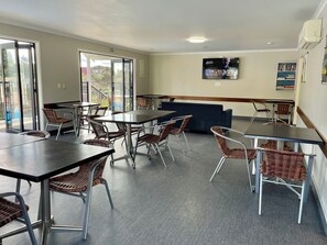 A modern dining area with tables and wicker chairs, a blue sofa, and a flat-screen TV on the wall.