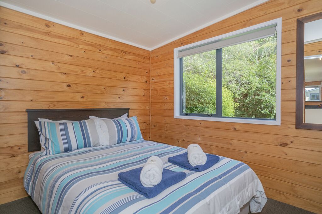 A wooden-paneled bedroom with a large window, a bed with striped bedding, and two towels on the bed.