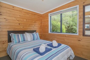 A wooden-paneled bedroom with a large window, a bed with striped bedding, and two towels on the bed.