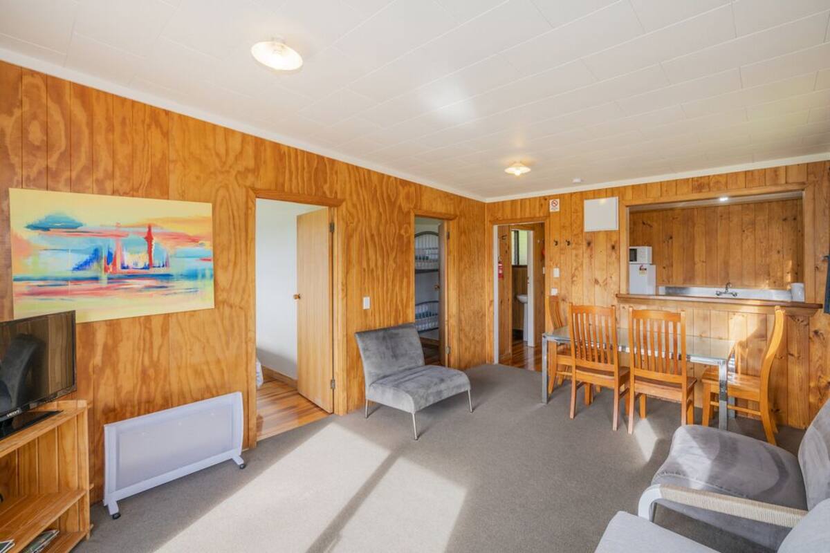 Un intérieur en bois comprenant un coin repas, un fauteuil gris, un canapé et un tableau au mur.