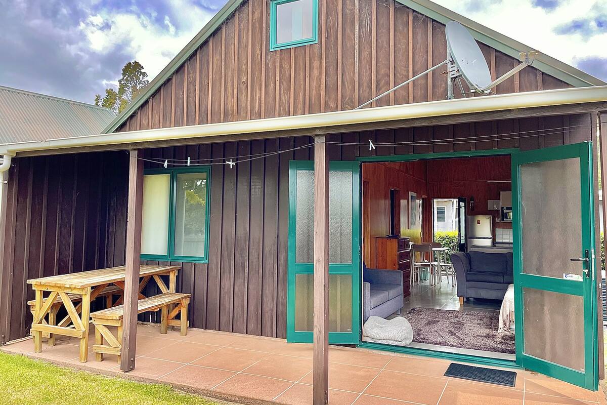 Une maison en bois avec un patio couvert, une table à manger et un canapé bleu.