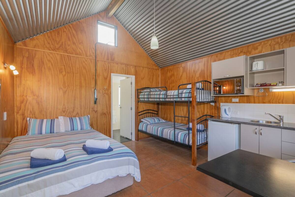 Une cabane en bois avec un lit superposé, un lit simple, une kitchenette et une salle de bain.