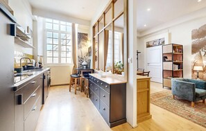 A modern kitchen with a central island, a dining area with a blue sofa, and a bookshelf. - 1 bedroom cozy apartment in Lons-Le-Saunier (Lons-Le-Saunier)