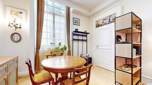 A dining area with a round wooden table and chairs, a bookshelf, and a window with curtains. - 1 bedroom cozy apartment in Lons-Le-Saunier (Lons-Le-Saunier)