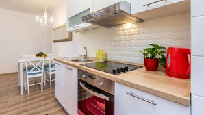Une cuisine moderne avec des meubles blancs, une hotte en acier inoxydable, un four encastré et une bouilloire rouge.