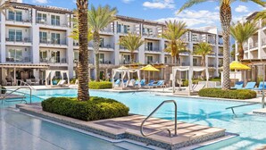 Ein Hotelpoolbereich mit mehreren Balkonebenen, Palmen und Liegestühlen.