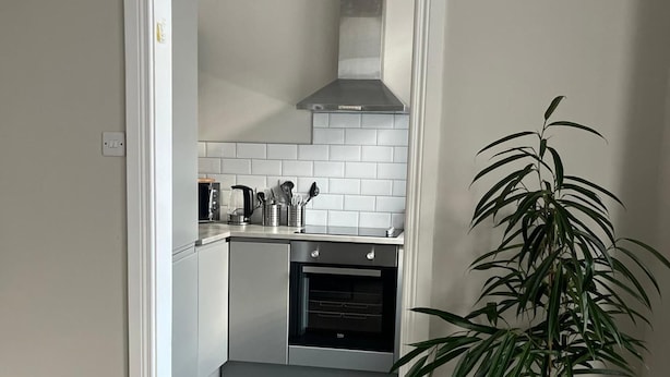 Een kleine keuken met witte tegels, een inbouwoven en een roestvrijstalen afzuigkap.
