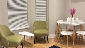 Een kamer met twee groene fauteuils, een witte bijzettafeltje en een eettafel met stoelen.