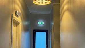 Een gang met een deur aan het einde, een nooduitgang en een plafondlamp.