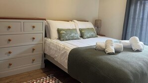 Een net opgemaakt bed met witte en groene beddengoed, een bedlampje en een klein nachtkastje.