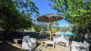 An outdoor seating area with a thatched umbrella, wicker furniture, and a view of a swimming pool in the background. - Pet friendly apartment (Gualdo Cattaneo)