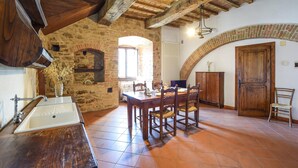A rustic kitchen with exposed brick walls, wooden beams, a large wooden table, and a stone fireplace. - Pet friendly apartment (Gualdo Cattaneo)