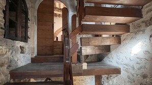 A spiral staircase in a stone-walled room with wooden beams and a wooden door at the top. - Pet friendly apartment (Gualdo Cattaneo)