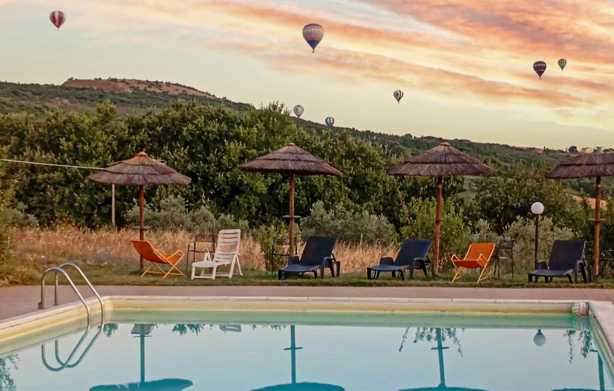 Una piscina con tumbonas y sombrillas, rodeada de vegetación y colinas.