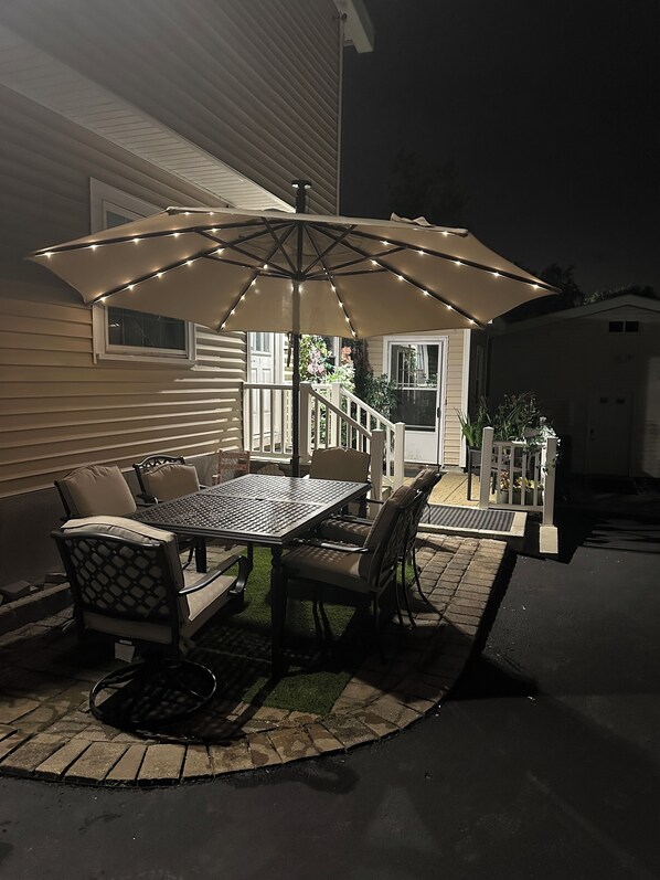 An outdoor patio with a table and chairs, a large umbrella, and a house in the background.