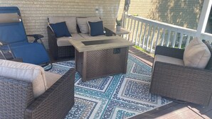 Un patio cubierto con mobiliario de mimbre, una alfombra estampada y una pared de ladrillo.