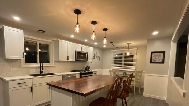 Una cocina moderna con armarios blancos, una isla de madera e iluminación colgante.