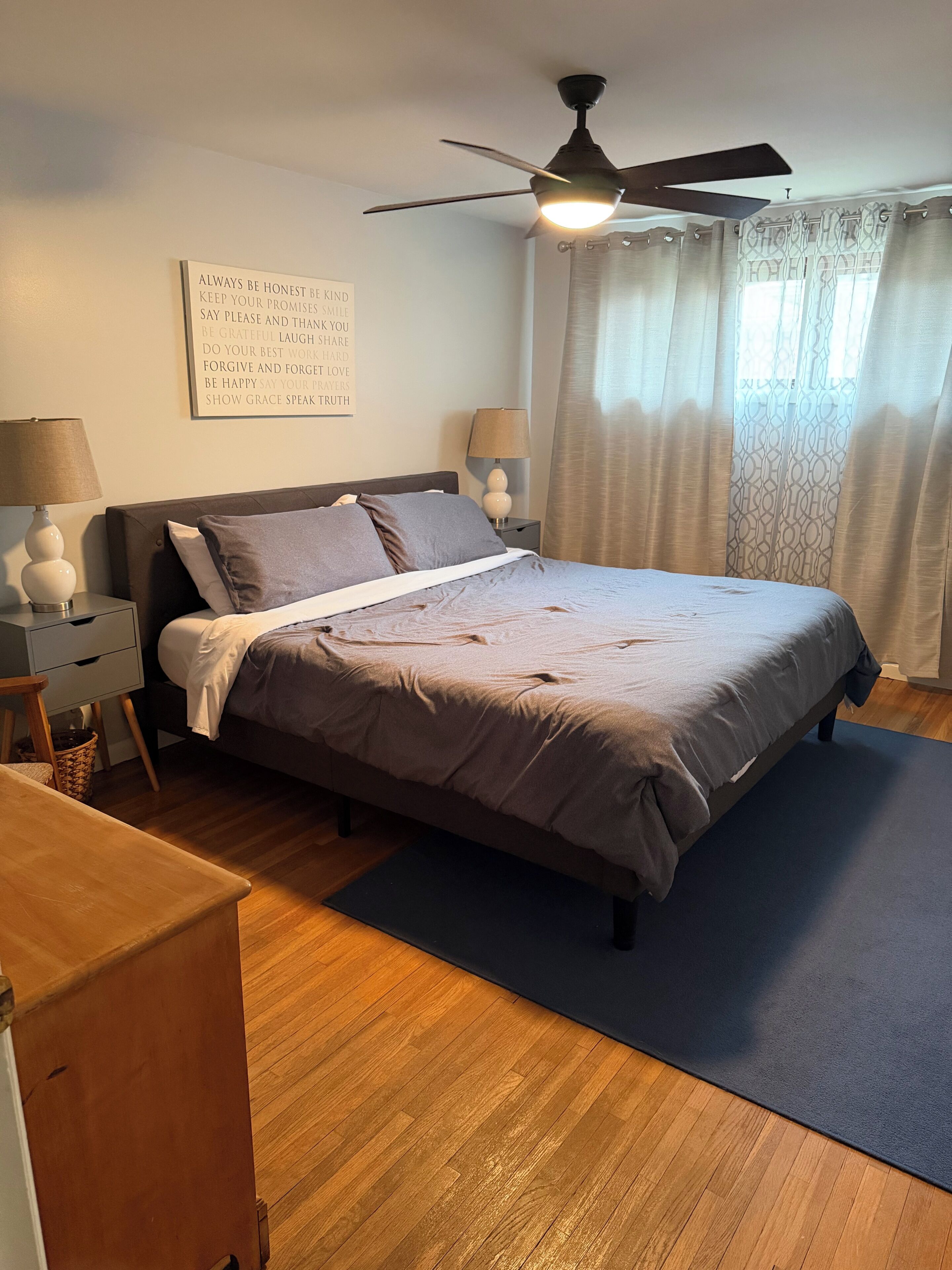 A bedroom with a bed, nightstands, a ceiling fan, and a motivational quote on the wall.