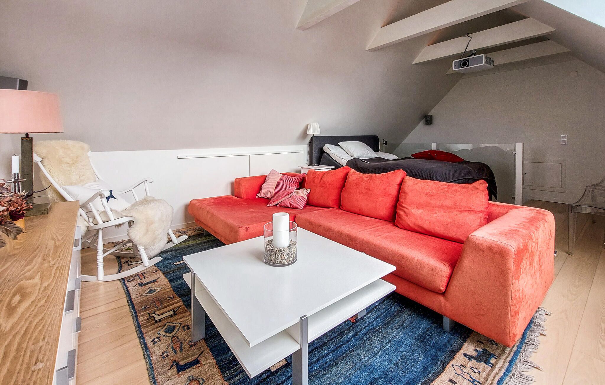 Un salon moderne avec un canapé rouge, une table basse blanche, un fauteuil blanc et un tapis à motifs bleus.