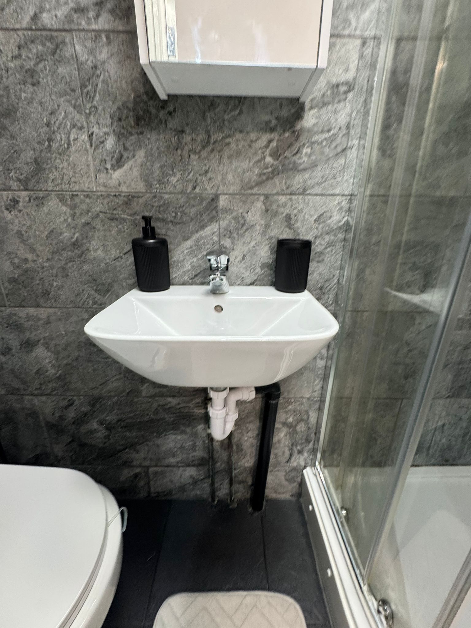 A bathroom with a white sink, black soap dispensers, and a glass shower enclosure.