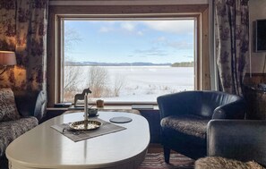 A room with a large window offering a view of a frozen lake and trees, a round table with a metal tray, and two leather chairs. - Amazing home in Mora with sauna (Mora)