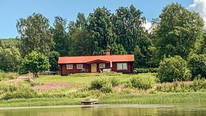 Una casa vermella amb un llumí, envoltada de vegetació exuberant i un cos d'aigua.