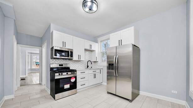Una cocina moderna con armarios blancos, electrodomésticos de acero inoxidable y un salpicadero con diseño tipo espiga.