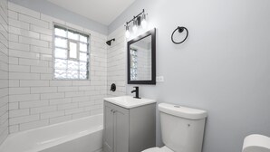 Un baño moderno con azulejos blancos, una bañera, un inodoro y un lavamanos con espejo.