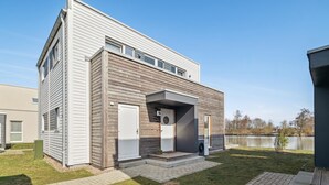 Une maison moderne à deux étages, dotée d’un toit plat, d’un porche couvert et d’un petit jardin à l’avant, avec un chemin pavé.