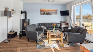 Un salon moderne avec un canapé gris, une table basse en bois et un tableau représentant un coucher de soleil sur la mer.