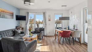 Un salon moderne avec un canapé gris, une table à manger avec des chaises et un téléviseur fixé au mur.