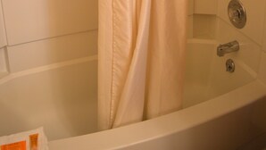Una bañera blanca con cortina de ducha, cabezal de ducha manual y un estante pequeño en la parte superior.