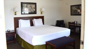 Una habitación de hotel con una cama grande, lámparas de noche, un escritorio con silla y un televisor.