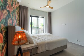 Un dormitorio con cama, ventilador de techo, ventana con cortinas e impresión tropical en la pared.