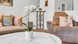 A living room with a sofa, armchair, and a coffee table. There is a plant on the coffee table and a shelf with decorative items. - 3-bedroom house in charming College Park with WiFi, AC /ATL airport 10 minutes (College Park)