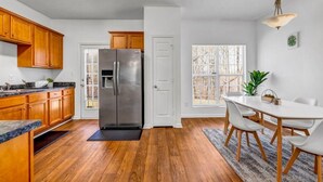 A modern kitchen with wooden cabinets, a stainless steel refrigerator, and a dining area with a white table and chairs. - 3-bedroom house in charming College Park with WiFi, AC /ATL airport 10 minutes (College Park)