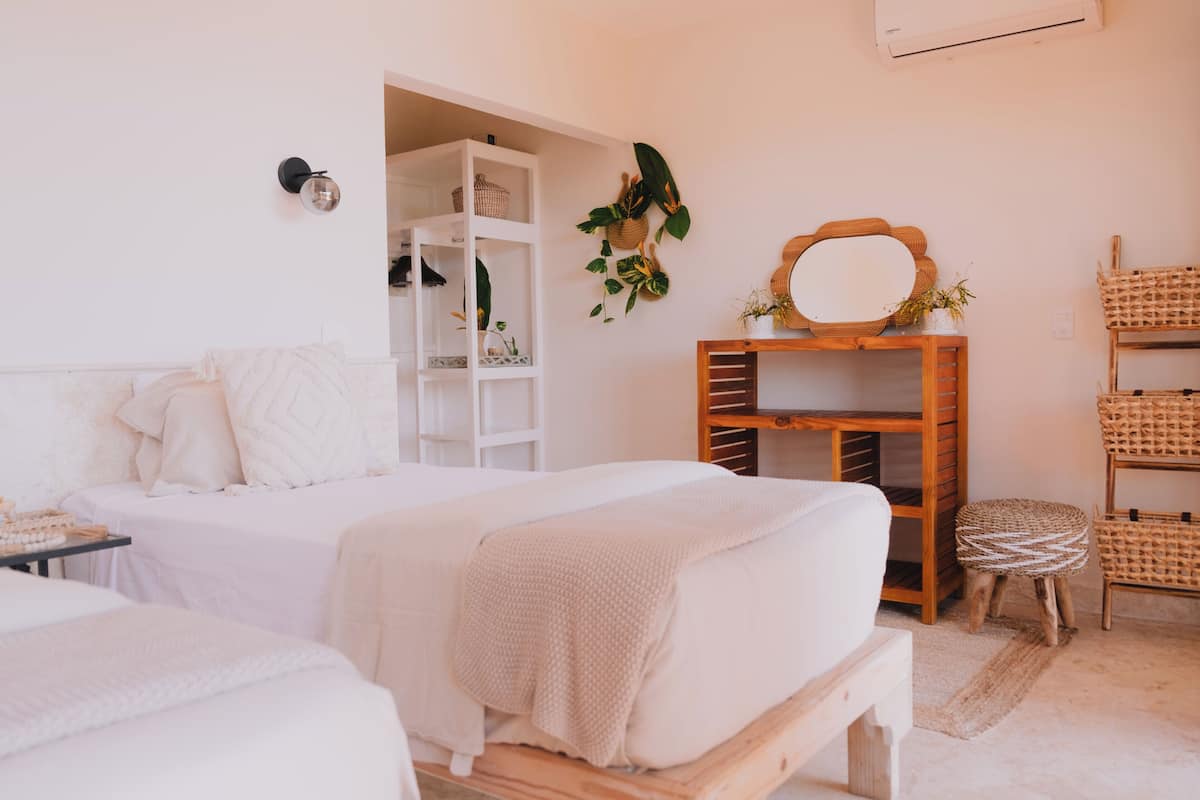 Un dormitorio con una cama, un banco de madera, un armario blanco y un espejo sobre un soporte de madera.