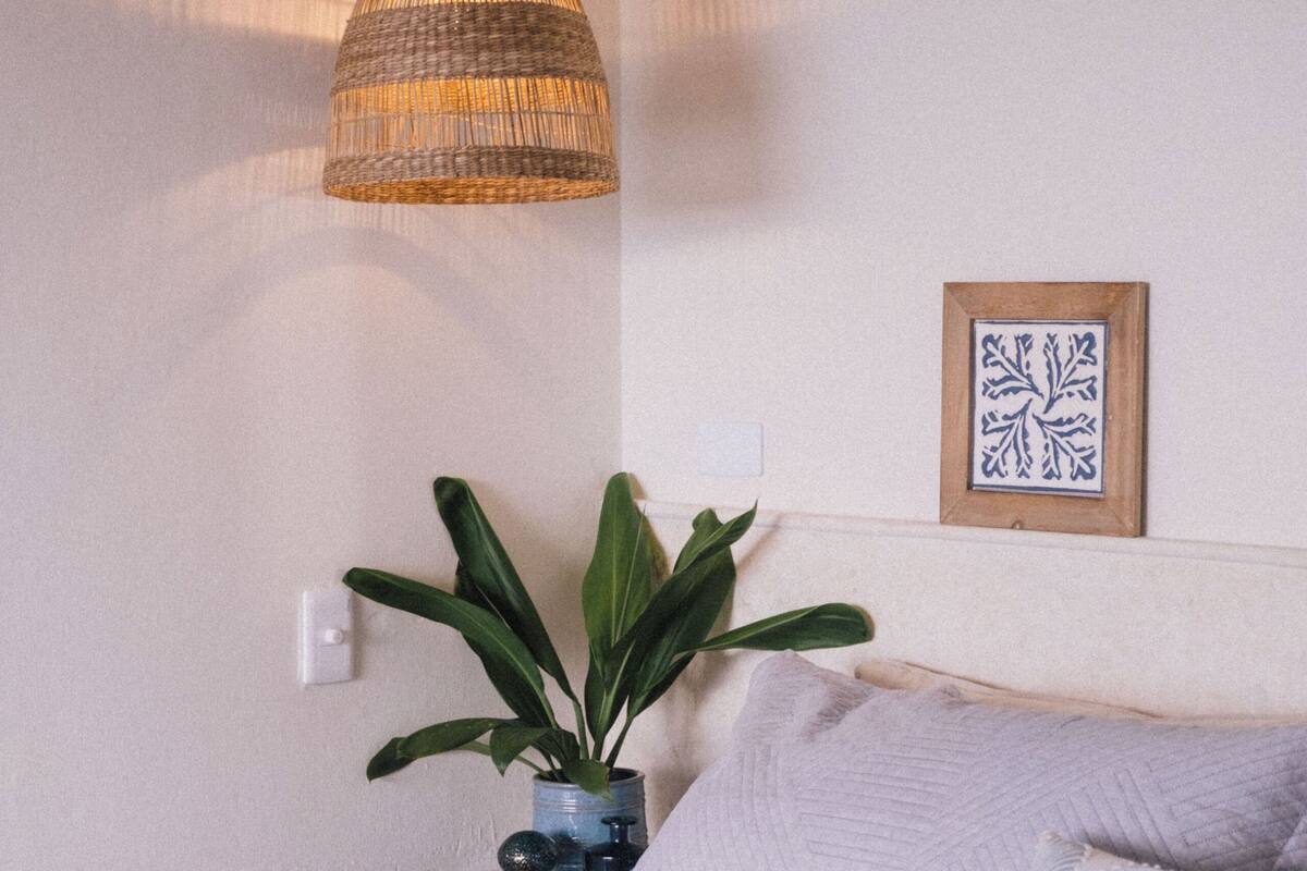 Un dormitorio con cama, lámpara colgante, planta en maceta y un cuadro en la pared.