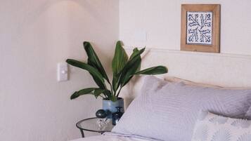 Un dormitorio con cama, lámpara colgante, planta en maceta y un cuadro en la pared.