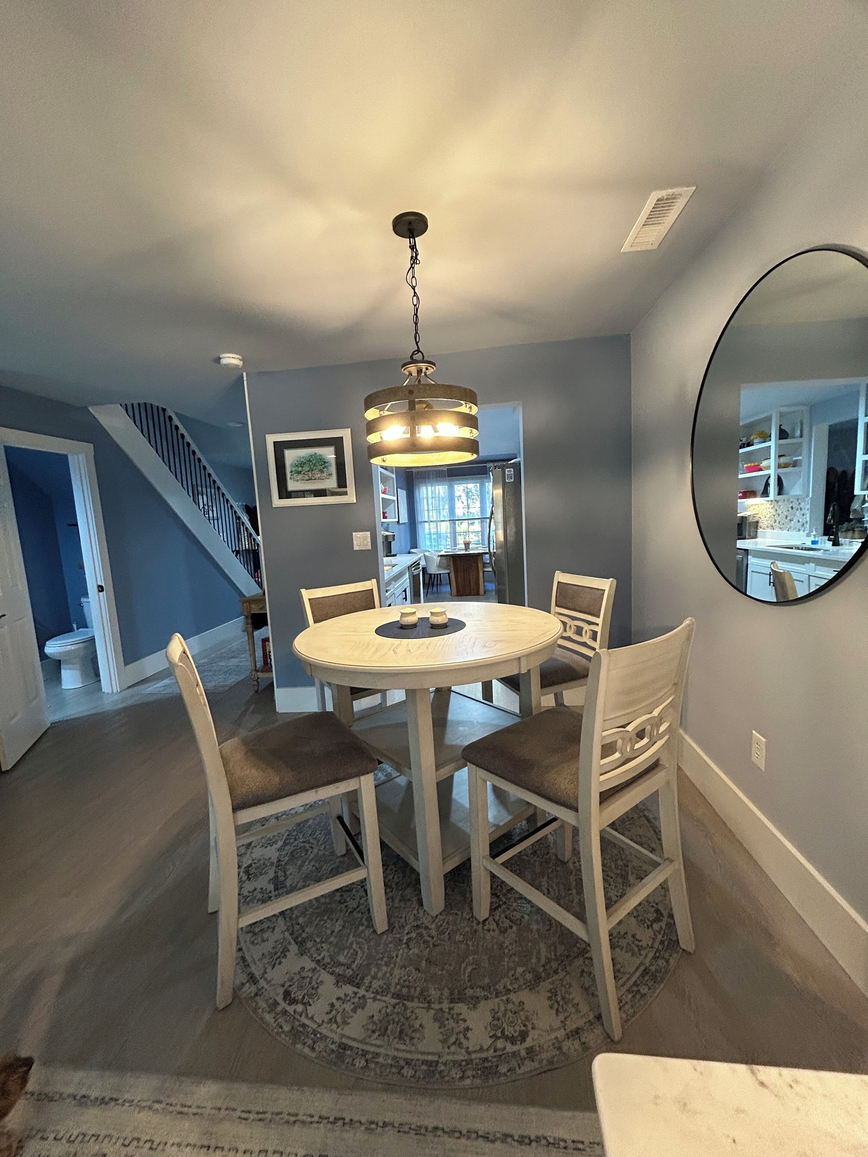A dining area with a round table, four chairs, and a hanging light fixture.